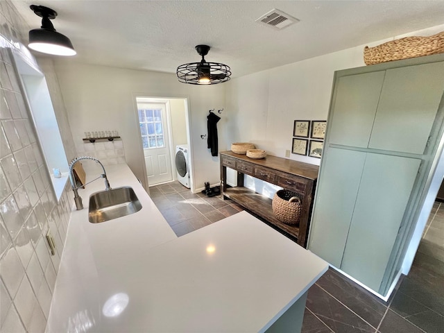 kitchen with washer / dryer, sink, green cabinetry, a textured ceiling, and kitchen peninsula