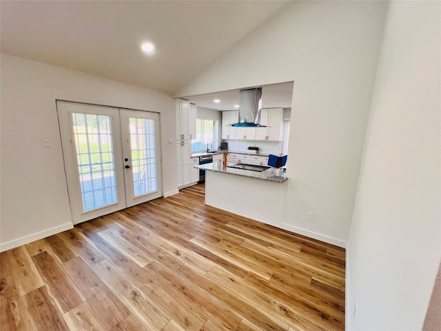 kitchen with white cabinets, light hardwood / wood-style floors, kitchen peninsula, wall chimney range hood, and french doors