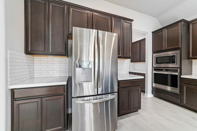 kitchen featuring dark brown cabinets, appliances with stainless steel finishes, decorative backsplash, and light wood-type flooring