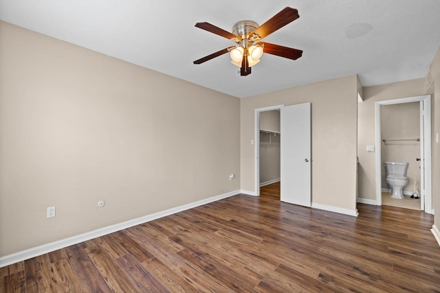 unfurnished bedroom featuring a closet, dark wood-type flooring, ceiling fan, and a spacious closet