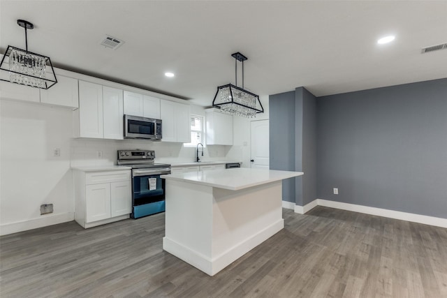 kitchen with a kitchen island, appliances with stainless steel finishes, pendant lighting, white cabinetry, and sink