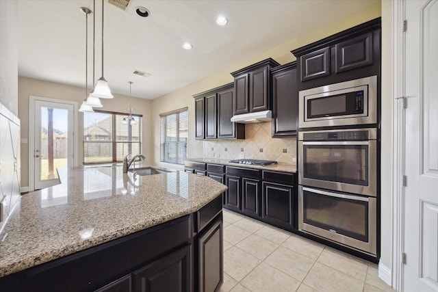 kitchen with sink, light stone counters, decorative light fixtures, stainless steel appliances, and backsplash