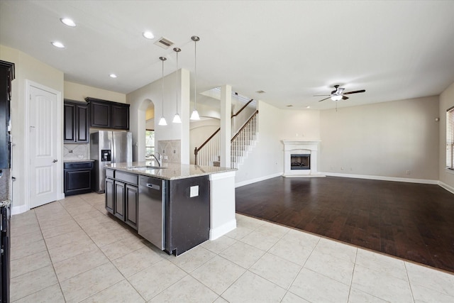 kitchen featuring stainless steel appliances, an island with sink, hanging light fixtures, and light tile patterned floors