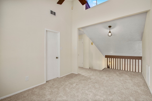 carpeted empty room featuring ceiling fan, a skylight, and a towering ceiling