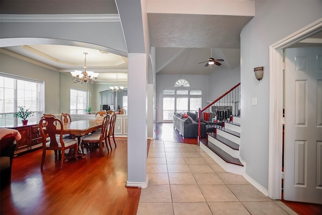 tiled entrance foyer featuring crown molding, a raised ceiling, and ceiling fan with notable chandelier