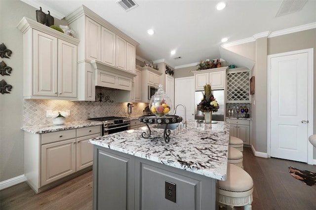 kitchen featuring appliances with stainless steel finishes, dark hardwood / wood-style flooring, a kitchen bar, a kitchen island with sink, and light stone counters