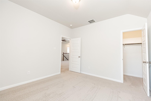 unfurnished bedroom with a walk in closet, a closet, and light carpet