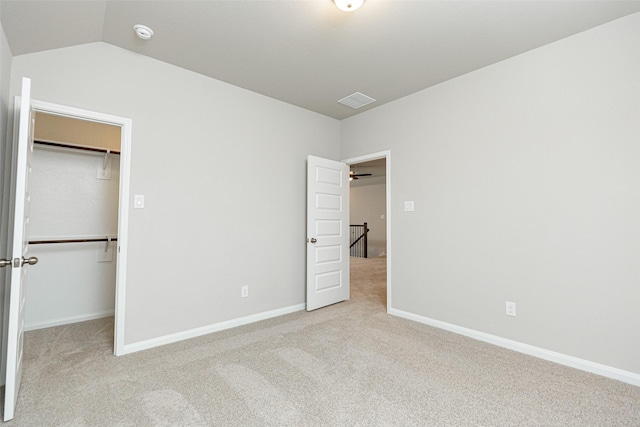 unfurnished bedroom featuring light colored carpet, lofted ceiling, a closet, and a walk in closet