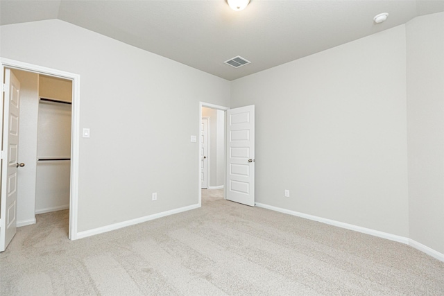 unfurnished bedroom featuring a walk in closet, light colored carpet, and lofted ceiling