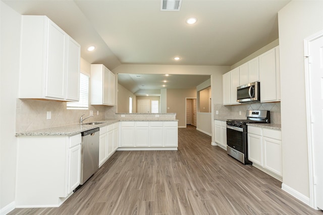 kitchen featuring white cabinets, light stone counters, kitchen peninsula, stainless steel appliances, and light hardwood / wood-style floors