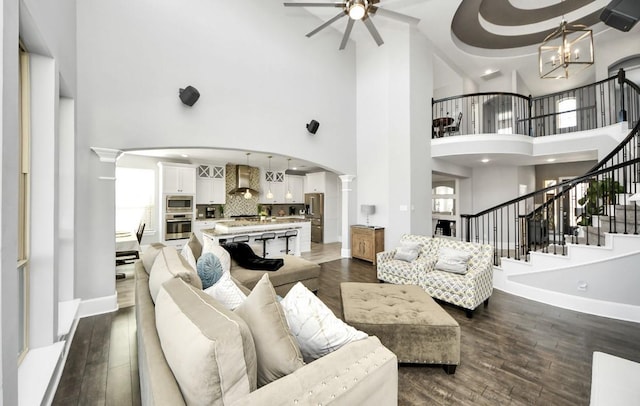 living room with ceiling fan with notable chandelier, a towering ceiling, dark hardwood / wood-style floors, and decorative columns