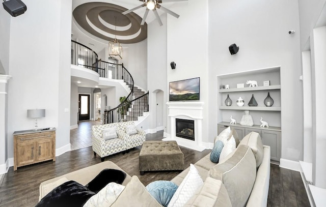 living room with dark hardwood / wood-style floors, ceiling fan with notable chandelier, and built in features