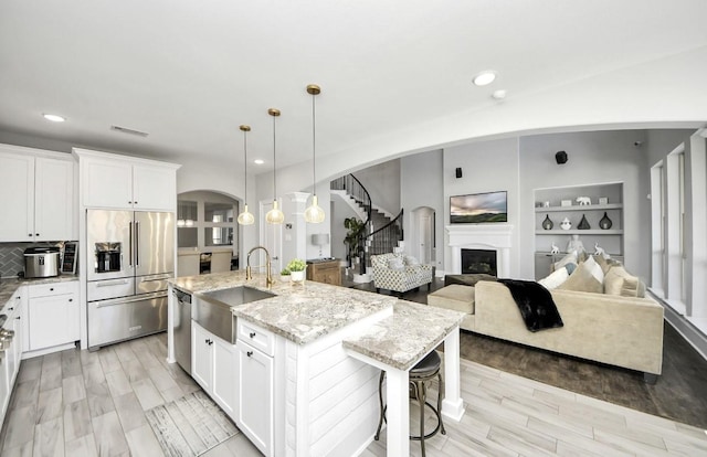 kitchen featuring stainless steel appliances, an island with sink, hanging light fixtures, and white cabinetry