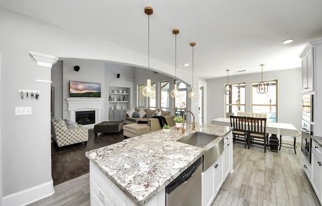 kitchen featuring an island with sink, sink, white cabinets, stainless steel appliances, and built in shelves