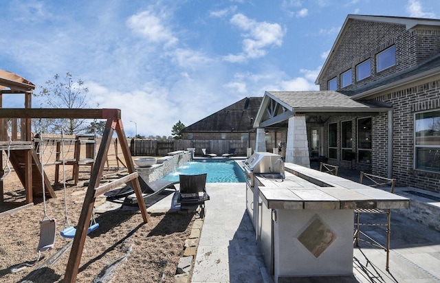 view of swimming pool featuring an outdoor bar, a playground, area for grilling, pool water feature, and exterior kitchen