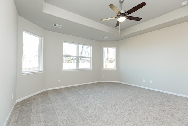 unfurnished room featuring ceiling fan, light colored carpet, a healthy amount of sunlight, and a tray ceiling