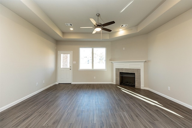 unfurnished living room with a tray ceiling, dark wood-type flooring, a tile fireplace, and ceiling fan