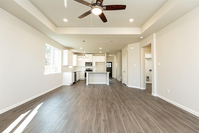 unfurnished living room featuring a tray ceiling, dark hardwood / wood-style flooring, and ceiling fan with notable chandelier