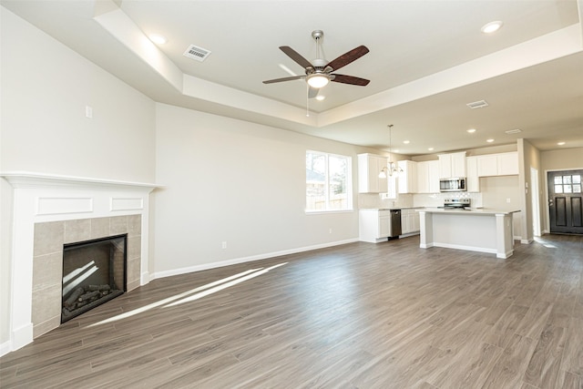 unfurnished living room featuring ceiling fan with notable chandelier, hardwood / wood-style floors, a fireplace, and a tray ceiling