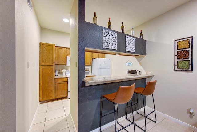 kitchen featuring light tile patterned floors, white appliances, a breakfast bar, a towering ceiling, and kitchen peninsula