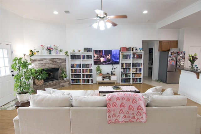 living room with ornamental molding, ceiling fan, a fireplace, and light hardwood / wood-style flooring