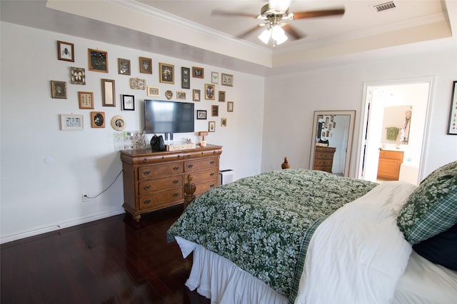 bedroom with connected bathroom, dark hardwood / wood-style flooring, ceiling fan, a raised ceiling, and crown molding