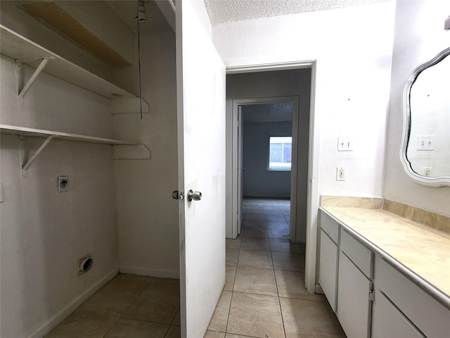 washroom with electric dryer hookup, light tile patterned floors, cabinets, and a textured ceiling