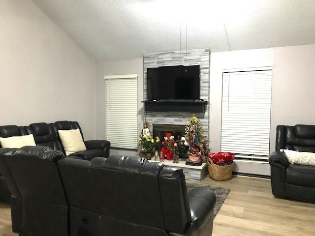 living room with a tiled fireplace, vaulted ceiling, a textured ceiling, and light hardwood / wood-style flooring