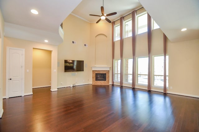 unfurnished living room with a tiled fireplace, a high ceiling, dark wood-type flooring, and ceiling fan