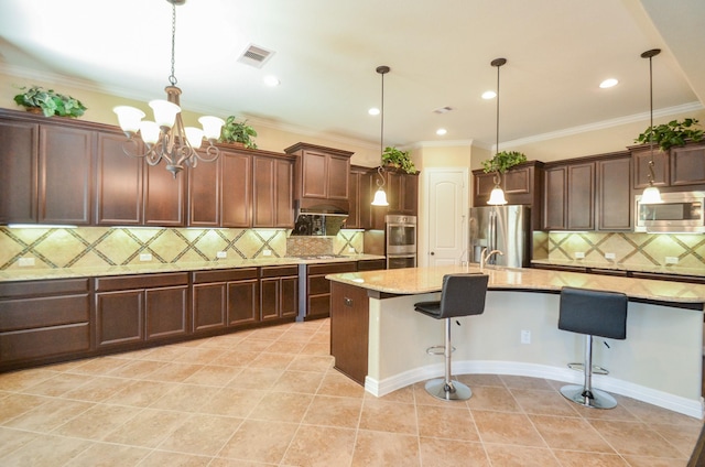 kitchen with hanging light fixtures, appliances with stainless steel finishes, a kitchen island with sink, and a kitchen bar