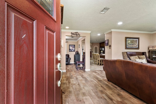 foyer entrance with ornamental molding, a textured ceiling, and light hardwood / wood-style floors