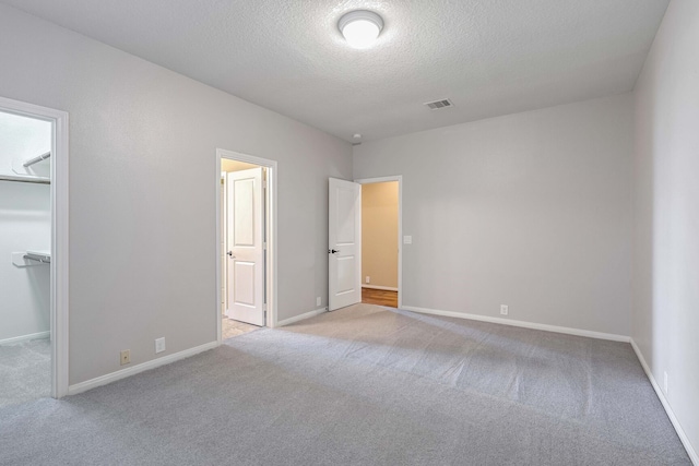 unfurnished bedroom with light carpet, a spacious closet, a closet, and a textured ceiling