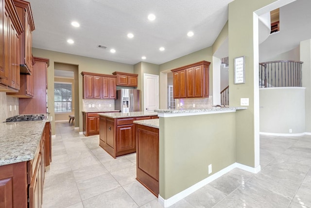 kitchen featuring tasteful backsplash, stainless steel appliances, a center island, and light stone countertops