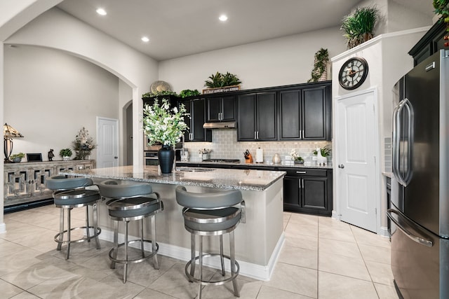 kitchen featuring light stone counters, appliances with stainless steel finishes, a breakfast bar, and a kitchen island with sink