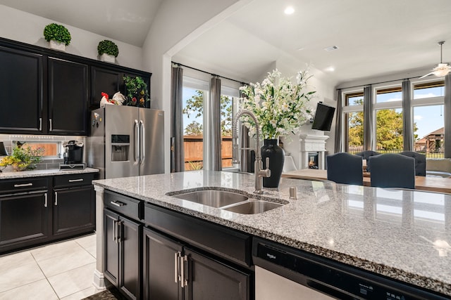 kitchen featuring lofted ceiling, sink, light stone counters, light tile patterned floors, and appliances with stainless steel finishes