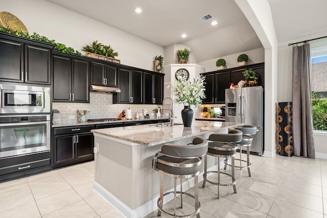 kitchen featuring appliances with stainless steel finishes, sink, a kitchen island with sink, light tile patterned floors, and light stone countertops