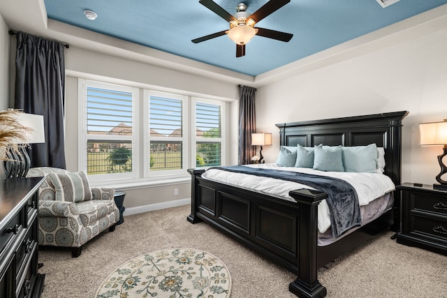 carpeted bedroom with a raised ceiling and ceiling fan