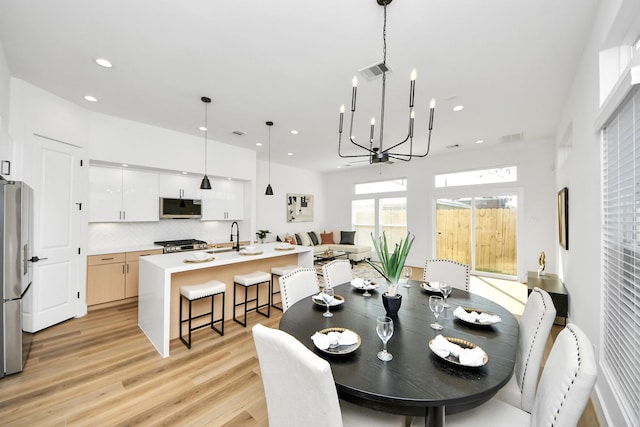 dining area with sink, light hardwood / wood-style flooring, and a notable chandelier