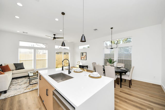 kitchen with sink, decorative light fixtures, stainless steel dishwasher, a kitchen island with sink, and light hardwood / wood-style floors