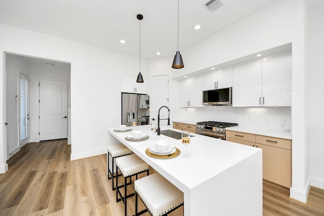 kitchen with pendant lighting, sink, stainless steel appliances, white cabinets, and a center island with sink