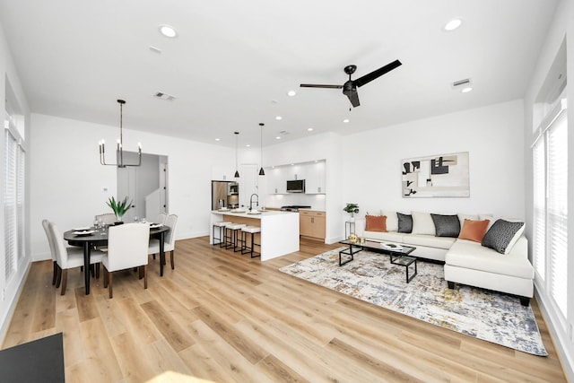 living room with ceiling fan with notable chandelier, sink, and light wood-type flooring