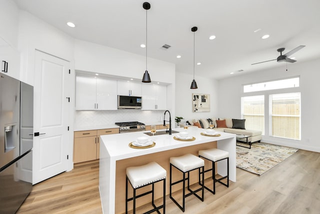 kitchen with sink, white cabinetry, hanging light fixtures, stainless steel appliances, and an island with sink