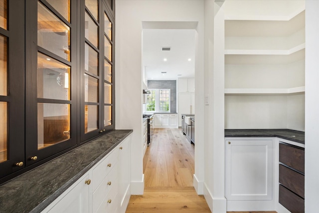 bar with stainless steel range with gas stovetop, light hardwood / wood-style flooring, dark stone counters, and white cabinets