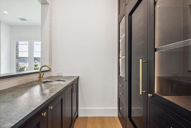 bar with dark stone countertops, sink, dark brown cabinets, and light hardwood / wood-style floors