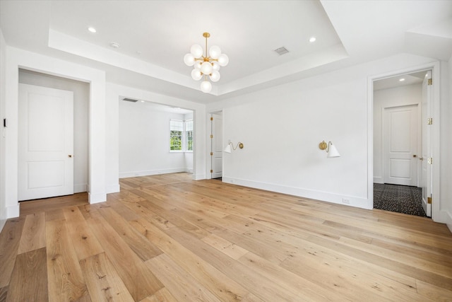 unfurnished room with light hardwood / wood-style flooring, an inviting chandelier, and a tray ceiling