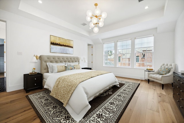 bedroom with a chandelier, a raised ceiling, and light hardwood / wood-style floors