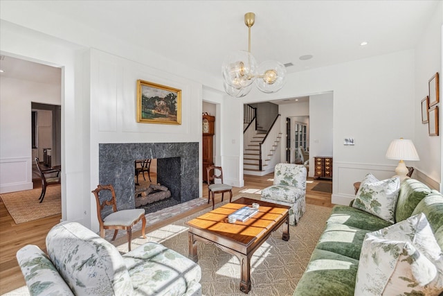 living room featuring an inviting chandelier, a high end fireplace, and light hardwood / wood-style flooring