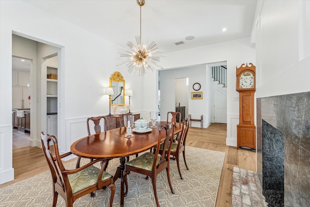 dining area featuring a tiled fireplace, a notable chandelier, and light hardwood / wood-style flooring