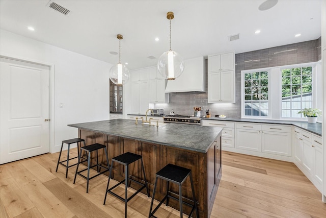 kitchen featuring range, white cabinetry, hanging light fixtures, an island with sink, and custom exhaust hood