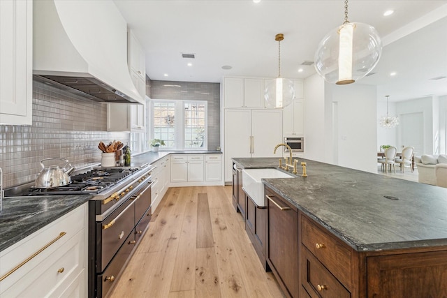 kitchen featuring premium range hood, pendant lighting, white cabinetry, sink, and double oven range